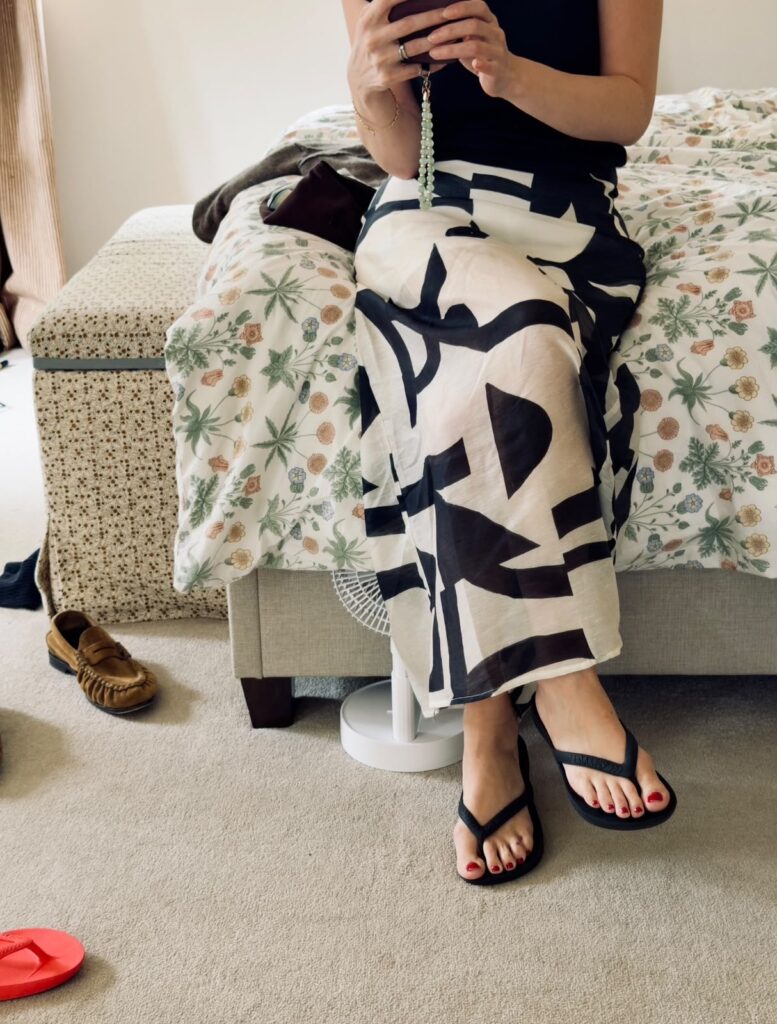 sophie in black and white skirt sat on bed, red flip flops